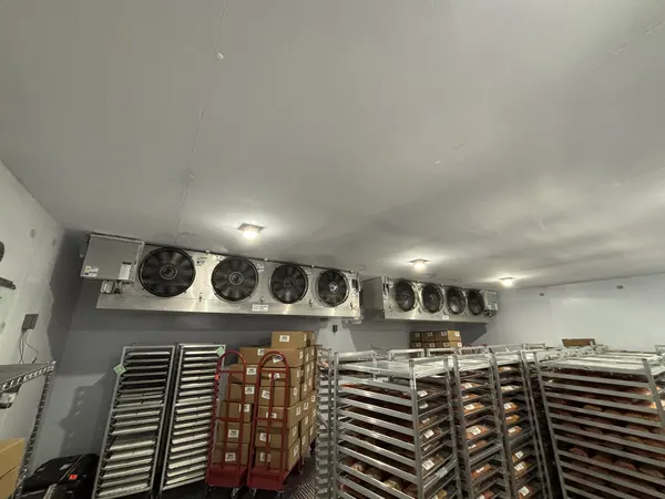 Walk-in cooler interior with evaporator fans above stocked storage racks
